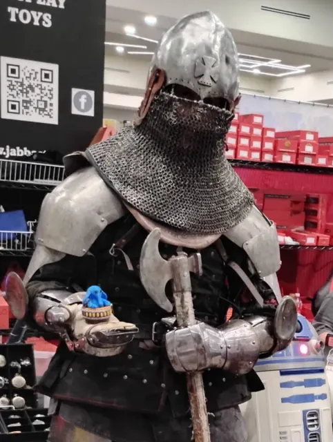 A person in a steel helmet, chainmail and plate armour holding a small blue Max Rebo figure in one gauntlet.